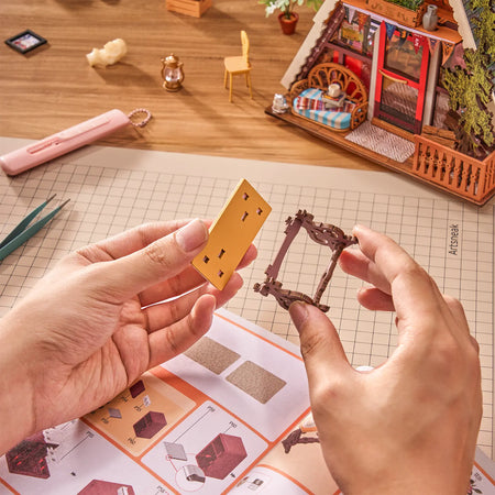 Een persoon zet een meubeltje van de Robotime A-Frame Cabin in elkaar