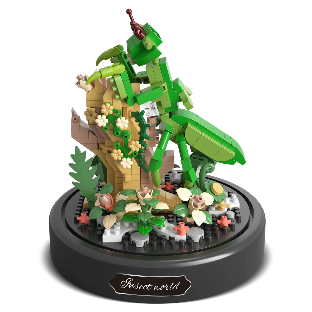 Productfoto van de Balody miniblocks bidsprinkhaan op een tak met bloemetjes en een met plantjes bedekte grond, onder een stolp